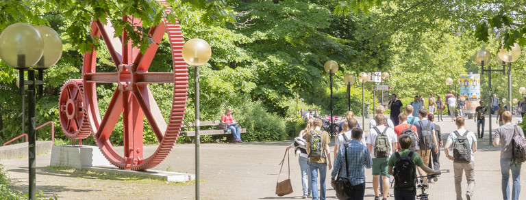 Students in summer on the North Campus, red cogwheels in the background