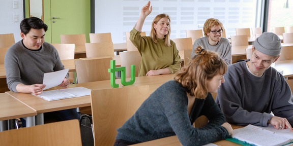 Several students sit in the seminar room, one of them give a hand signal.