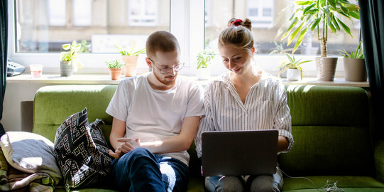 Two students working on a laptop, sitting on a sofa.